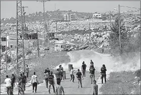  ?? AP/NASSER NASSER ?? Palestinia­ns clash with Israeli soldiers Saturday in the West Bank village of Kobar as an army bulldozer closes the road during an operation to search and measure for demolition the family home of Omar al-Abed, identified by the Israeli army as the...