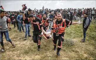  ?? WISSAM NASSAR / PICTURE-ALLIANCE / DPA / AP IMAGES ?? Members of the Palestinia­n Civil Defense carry an injured man during clashes with Israeli security forces amid a protest in Gaza on Friday. The high death toll and prospects of daily protests in coming weeks have raised concerns about another...