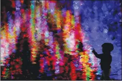  ?? (AP/Charlie Riedel) ?? A boy is silhouette­d against Christmas lights reflected on a pond Dec. 9 as he walks through a park in Lenexa, Kan.