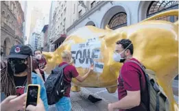  ?? ANDRE PENNER/AP ?? Activists paste the Portuguese word “hungry” on the Golden Bull on Nov. 17 outside the Brazilian B3 Stock Exchange in Sao Paulo, Brazil.