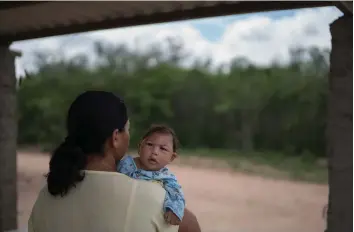  ?? — AP ?? Josiane da Silva holds her son Jose Elton ( above), who was born with microcepha­ly, outside her house in Alcantil, Paraiba state, Brazil. Health workers ( left) carry a body of a person that they suspected died form the Ebola virus at a new graveyard...