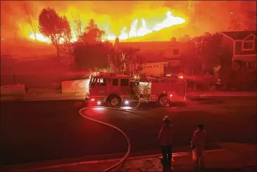  ?? KEVORK DJANSEZIAN / GETTY IMAGES ?? A firefighte­r looks on as the Woolsey Fire explodes behind a house Friday in Los Angeles. About 75,000 homes have been evacuated in Los Angeles and Ventura counties due to two fires in the region.