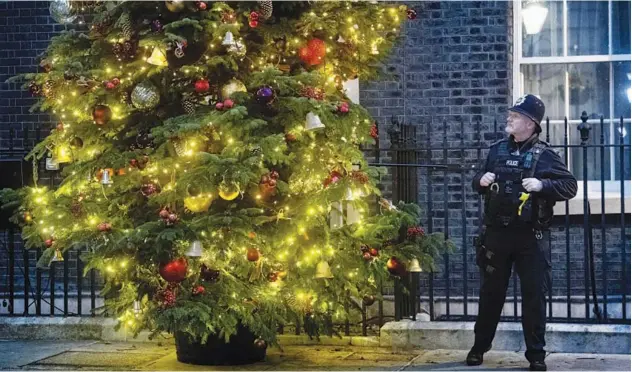  ?? Associated Press ?? ↑
A policeman looks at the decoration­s on the Christmas tree outside 10 Downing Street in London on Sunday.