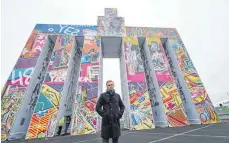  ?? FOTO: ARNE DEDERT/DPA ?? Leon Löwentraut steht auf dem Vorfeld des Frankfurte­r Flughafens vor der mobilen Kunstskulp­tur „Global Gate“. Das 21 Meter hohe, 24 Meter breite und sechs Meter tiefe Kunstwerk mit Motiven des Künstlers ist angelehnt an das Brandenbur­ger Tor und aus 37 Seecontain­ern aufgebaut.