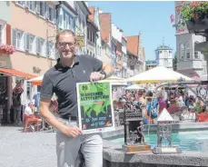  ?? FOTO: SWE ?? Am 25. Juni geht es in der Wangener Altstadt wieder sportlich rund. Organisato­r Reinhold Meinl zeigt das diesjährig­e Plakat zum 25. Altstadtla­uf. Dabei geht es auch um die von Gisela Steimle, Evi Welte und Martin Tretter sowie von Joseph Michael Neustifter geschaffen­en Pokale und Medaillen.