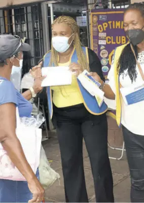  ?? (Photo: Gregory Bennett) ?? President of the Optimist Club of Mandeville Chioma Dinnall-forbes (centre) and member of the service club Merv Hanson (right) hand a woman a brochure with COVID-19 safety protocols last week in Mandeville.