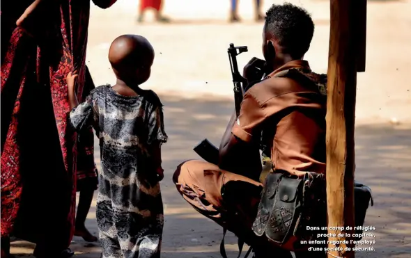  ??  ?? Dans un camp de réfugiés proche de la capitale, un enfant regarde l’employé d’une société de sécurité.