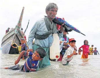  ??  ?? WEIGHED DOWN: A Rohingya refugee pulls a child as they walk to the shore after crossing the Bangladesh-Myanmar border by boat through the Bay of Bengal in Shah Porir Dwip, Bangladesh.