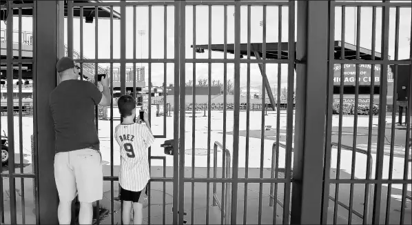  ?? SUE OGROCKI / AP ?? Cubs fans take photos through the locked gates at Sloan Park on March 13 in Mesa, Ariz. A day earlier, Major League Baseball canceled the rest of its spring training games and delayed the start of the season because of the coronaviru­s outbreak.