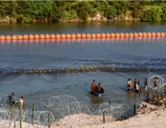  ?? SUZANNE CORDEIRO/AFP VIA GETTY IMAGES ?? Migrants walked by a string of buoys placed in the water along the US-Mexico Rio Grande border in Eagle Pass, Texas, on July 16.