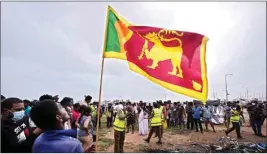  ?? PTI ?? A Sri Lankan man holds a national flag as police officers conduct investigat­ions into aftermath of clashes between government supporters and anti government protesters in Colombo, Sri Lanka, Tuesday