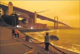  ?? ASSOCIATED PRESS FILE PHOTOS ?? This Sept. 9photo taken at 11:25a.m. shows people stopping near Fort Point to take photos of an orange sky over the Golden Gate Bridge caused by heavy smoke from wildfires in San Francisco.