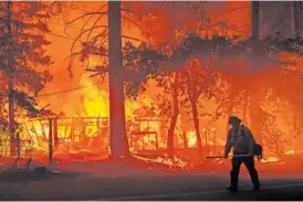  ?? AP PHOTO/NOAH BERGE ?? A firefighte­r passes a burning home Saturday as the Dixie Fire flares in Plumas County, Calif.