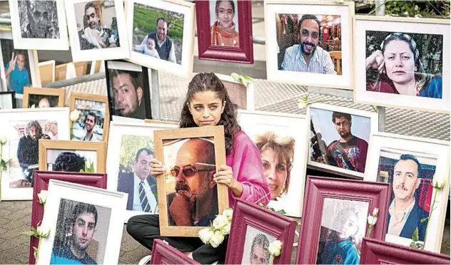  ?? Agence France-presse ?? Syrian campaigner Wafa Mustafa sits between pictures of victims of the Syrian regime as she holds a picture of her father, during a protest in Koblenz on Thursday.