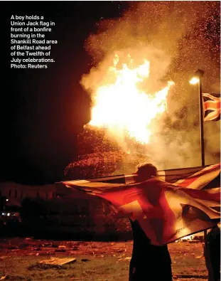  ??  ?? A boy holds a Union Jack flag in front of a bonfire burning in the Shankill Road area of Belfast ahead of the Twelfth of July celebratio­ns. Photo: Reuters
