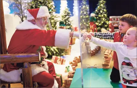  ?? Associated Press photos ?? Julianna and Dylan Lasczak, 3 and 5, visit with Santa through a transparen­t barrier at a Bass Pro Shop in Bridgeport on Nov. 10. Santa Claus is coming to the mall — just don’t try to sit on his lap. Malls are doing all they can to keep the jolly old man safe from the coronaviru­s, including banning kids from sitting on his knee, no matter if they’ve been naughty or nice.