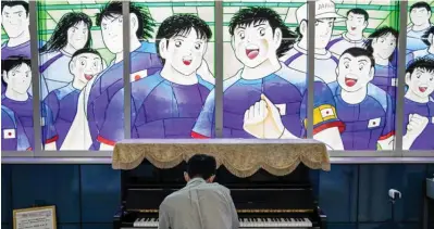  ?? ?? A train passenger plays piano next to stained glass artwork depicting the “Captain Tsubasa” anime cartoon at Urawa-Misono train station in Saitama on July 4, 2020.