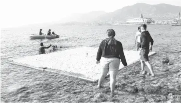  ?? — AFP photo ?? Greek university students gently deposit a wall-sized PVC frame on the surface before divers moor them at sea at a beach in the island of Lesbo.