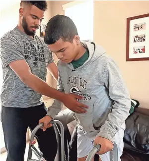  ?? CHERYL EVANS/THE REPUBLIC ?? Adrian Edwards, 19, helps his brother, Marcus, 15, walk with the help of a walker. Marcus Edwards hopes to play football again after brain-tumor surgery.