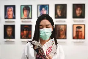  ??  ?? Thai artist Jinnipha Nivasabut reading the Japanese manga Naruto by Mavashi Kishimoto. In the background are oil portraits of deceased anime characters, at her exhibition The 2D Afterlife, at Palette Artspace in Bangkok.