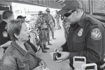  ??  ?? A U.S. Customs and Border Protection agent speaks with a Cuban asylumseek­er as newly arrived troops watch at Hidalgo’s internatio­nal bridge with Mexico.