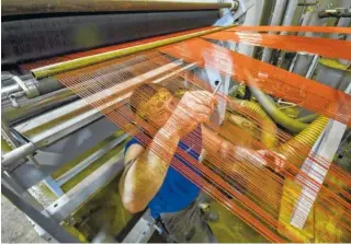  ??  ?? Above: Jason Durham separates colored synthetic fiber on a weaving machine inside the TenCate plant in Dayton.