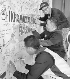  ??  ?? Participan­ts of the convoy sign their names on a banner as a pledge to fight corruption.