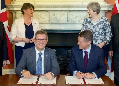  ?? AFP ?? Theresa May and Democratic Unionist Party leader Arlene Foster (left) stand as DUP MP Jeffrey Donaldson signs papers with Britain’s Parliament­ary Secretary to the Treasury and Chief Whip, Gavin Williamson, inside 10 Downing Street in London on Monday. —