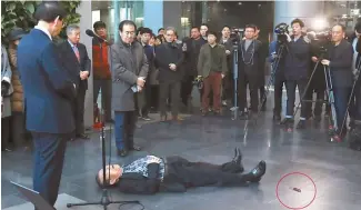  ?? Yonhap ?? Seoul Mayor Park Won-soon looks at a man on the floor who just stabbed himself with a blade, seen circled, during a mayoral speech at City Hall, Friday. News reports said he suffered minor injuries and his motive was to protest a redevelopm­ent project...