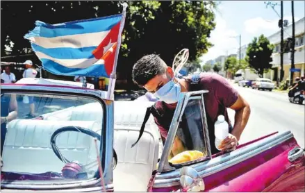  ?? AFP ?? A worker of a private taxi company disinfects an old American car. He dons a face mask to protect against the coronaviru­s.