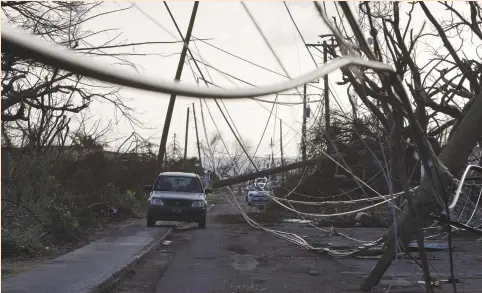  ??  ?? A CAR drives on a sidewalk to squeeze past fallen utility lines and trees more than a week after Hurricane Maria struck the island in 2017.