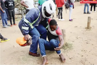  ?? Pic: Shepherd Tozvireva ?? A police officer helps a tout after he was hit by a car while running away from the law enforcemen­t agents along Seke Road in Harare yesterday
