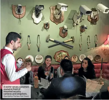  ?? (Dan Balilty/The New York Times) ?? A waiter serves customers seated in front of mounted security cameras and slingshots.