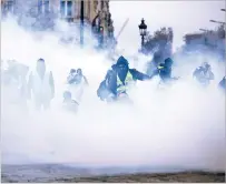  ?? KAMIL ZIHNIOGLU/ASSOCIATED PRESS ?? Masked demonstrat­ors wearing yellow jackets appear Saturday through tear gas near the Champs-Élysées avenue during a demonstrat­ion in Paris. French authoritie­s have deployed thousands of police to try to contain protests over rising taxes and Emmanuel Macron’s presidency.