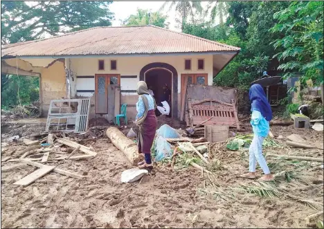  ??  ?? Indonesian women walk past a house damaged by flood in Waiwerang, on Adonara Island, East Nusa Tenggara province, Indonesia on April 6. (AP)