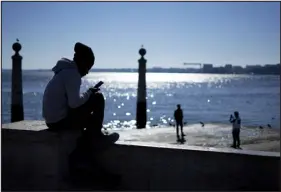  ?? ARMANDO FRANCA — THE ASSOCIATED PRESS ?? A young man checks his phone by the Tagus Rver at Lisbon’s Comercio Square on a sunny winter day on Jan. 30. A new tool aims to help teens take down explicit images and videos of themselves from the internet.