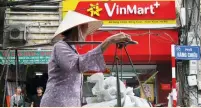  ?? (Kham/Reuters) ?? A WOMAN walks past a Vinmart shop in Hanoi on Monday.