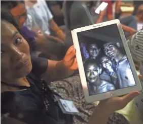  ?? LILLIAN SUWANRUMPH­A/AFP/GETTY IMAGES ?? A happy family member shows pictures of four of the 12 boys who were missing inside a cave complex in Thailand.