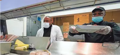  ?? AP ?? Andrew Walcott, left, owner of Fusion East Caribbean & Soul Food, monitors orders as chef Andrew Jackson works.