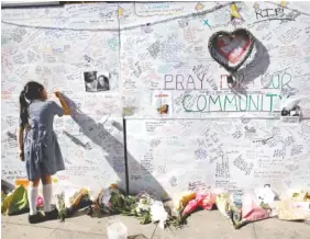  ?? THE ASSOCIATED PRESS ?? A school girl writes a message on a wall for the victims and in support for those affected by the massive fire in Grenfell Tower in London.