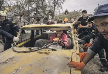  ?? EMERGENCY PERSONNEL Chris McGrath Getty Images ?? and residents of Zaporizhzh­ia in southeast Ukraine move a damaged car Friday after a Russian attack. Fighting continues to rage along a 300-mile front in the eastern Donbas area.