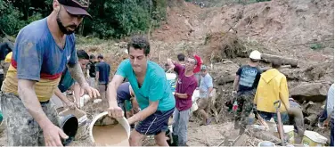  ?? Reuters ?? ↑
Residents carry buckets of mud and water as firefighte­rs dig for victims of a mudslide in Guaruja on Tuesday.