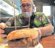  ??  ?? Justin “Nic” Nicholas photograph­s a burger before having it for lunch on the first day he reopened Nic's Place Diner and Lounge. [PHOTOS BY DAVE CATHEY/ THE OKLAHOMAN]