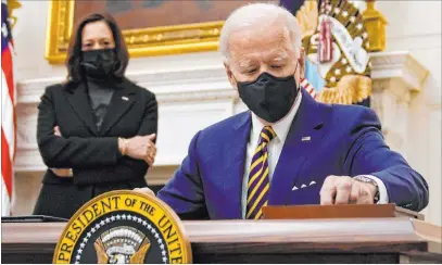  ?? Evan Vucci The Associated Press ?? President Joe Biden signs executive orders on the economy Friday in the State Dining Room of the White House; behind him is Vice President Kamala Harris. The orders speed financial relief to millions of Americans affected by the coronaviru­s pandemic.