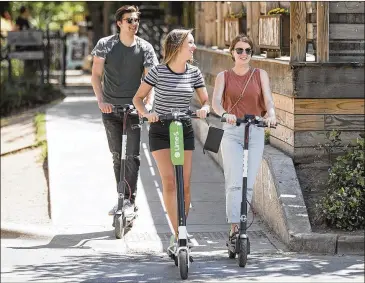  ?? RICARDO B. BRAZZIELL / AMERICAN-STATESMAN ?? Krista Meluci (center) leads the way last month on a LimeBike scooter as Vince Terrazas (left) and Sierra Medrano follow on Bird scooters down Rainey Street in downtown Austin. The city is implementi­ng a new licensing program for the transporta­tion...