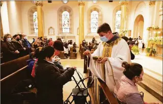  ?? Mark Lennihan / Associated Press ?? The Rev. Russels Governale serves communion on Sunday during a Spanish-language Easter service at St. Bartholome­w Roman Catholic Church in New York, which lost 80 of its members to COVID-19.