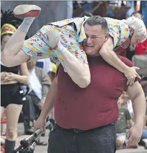  ?? ED KAISER ?? Busker Rob Williams of Kamikaze Fireflies scoops up Mitch Gray, a volunteer from the audience, to get on his shoulders to perform a fire juggling routine with colleague Casey Martin during the Street Performers Festival at Churchill Square last week.