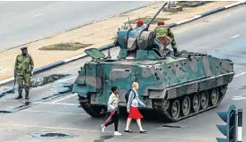  ?? /AFP Photo /Jekesai Njikizana ?? Life goes on: Young women walk past an armoured personnel carrier in Harare on Wednesday. Zimbabwe’s military appears to be in control of the country.