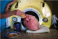  ?? Tribune News Service ?? ■ Caregiver and friend Kathryn Gaines feeds toast to Paul Alexander inside his iron lung April 27 at his home in Dallas. Now in his 70s, Alexander is one of the few people left who uses an iron lung to help facilitate breathing for those affected by...