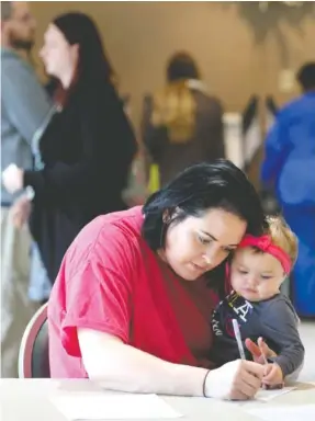  ?? STAFF PHOTO BY ERIN O. SMITH ?? Emily Johnson holds her 10-month-old daughter, Eleanor Johnson, as she fills out informatio­n before voting Tuesday at Rossville City Hall. The lines were fairly short at the precinct, however, there was a constant flow of voters throughout the day.